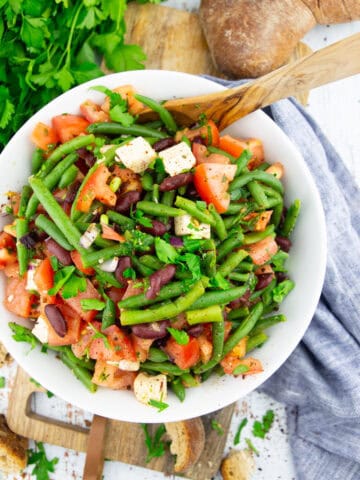 a white bowl with green bean salad with tomatoes and kidney beans on a wooden board