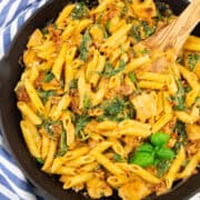 a cast iron pan with Tuscan pasta with sun-dried tomatoes and spinach on a white wooden board