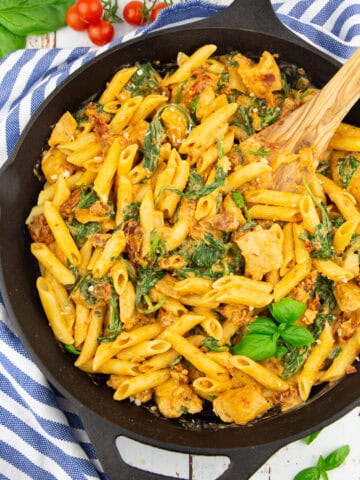 a cast iron pan with Tuscan pasta with sun-dried tomatoes and spinach on a white wooden board