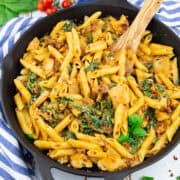 a cast iron pan with Tuscan pasta with sun-dried tomatoes and spinach on a white wooden board