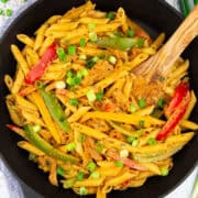 a cast iron skillet with pasta with bell pepper on a white wooden board