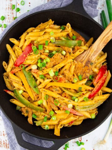 a cast iron skillet with pasta with bell pepper on a white wooden board