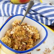 a blue and white bowl with millet porridge with a spoon with a pear and a cup of coffee in the background
