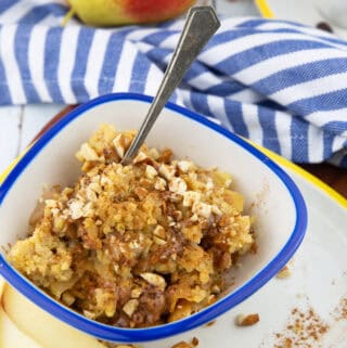 a blue and white bowl with millet porridge with a spoon with a pear and a cup of coffee in the background