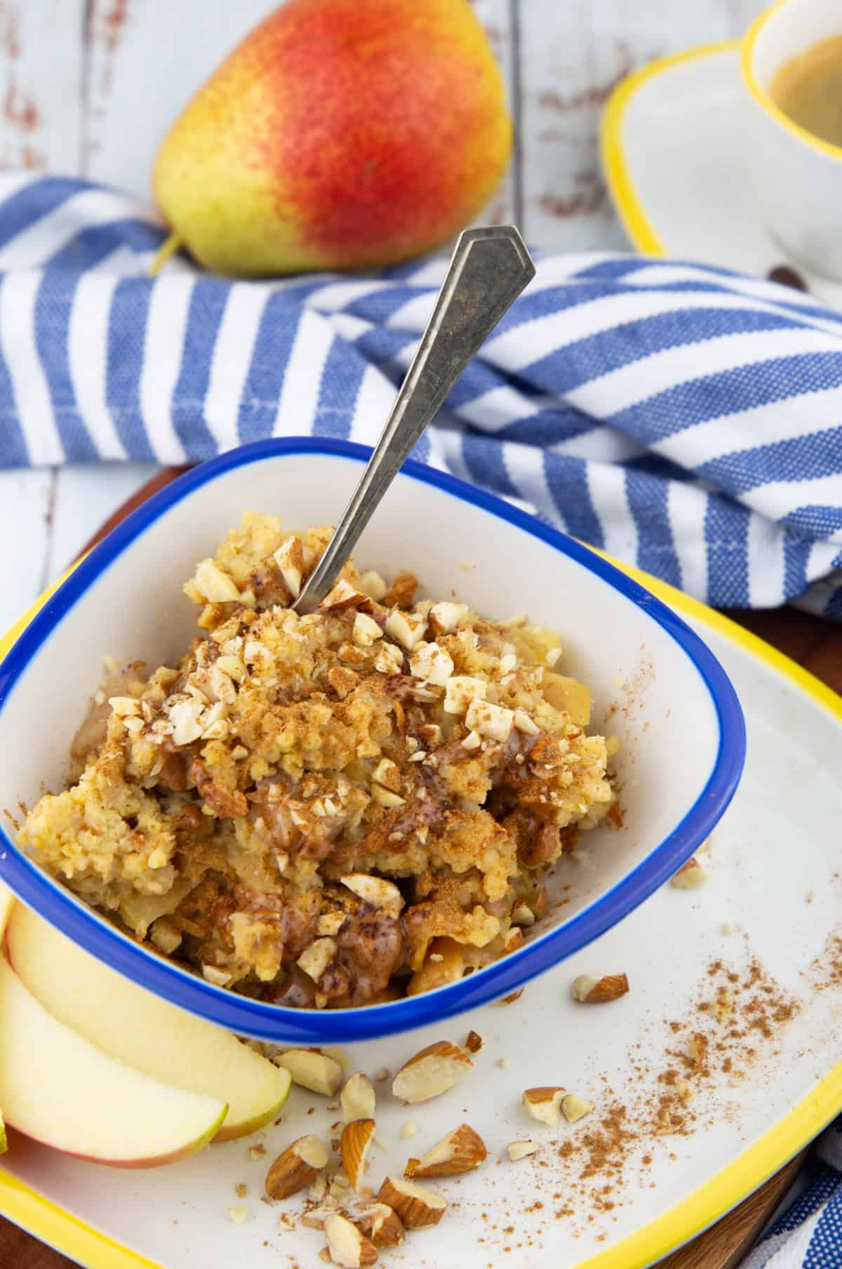 a blue and white bowl with millet porridge with a spoon with a pear and a cup of coffee in the background 