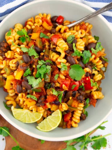 a grey plate with black bean pasta with bell pepper, lime wedges, and fresh cilantro on a wooden board