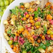 a white bowl with fall quinoa salad with sweet potato on a white wooden board with grapes in the background