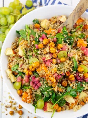 a white bowl with fall quinoa salad with sweet potato on a white wooden board with grapes in the background