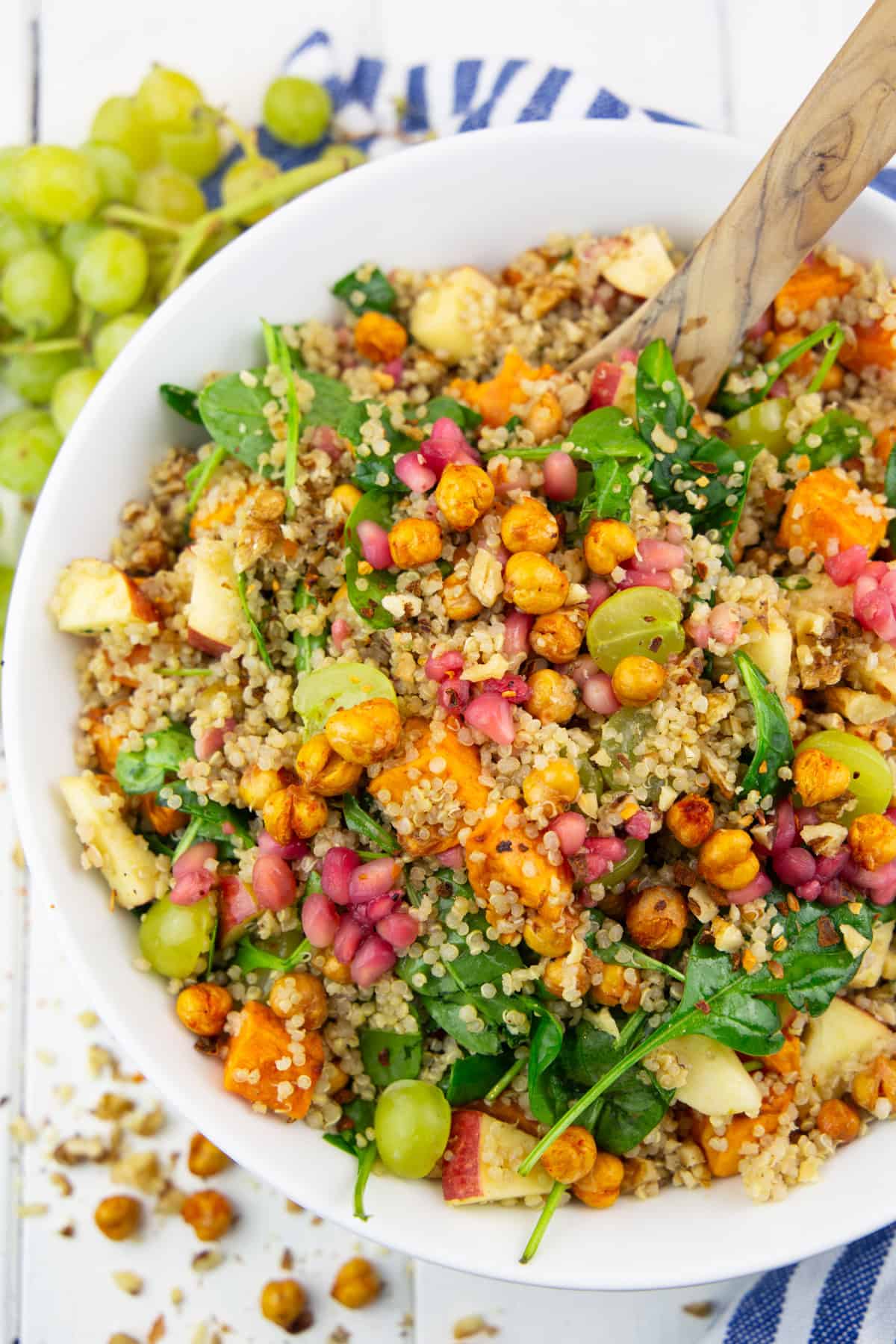 a white bowl with fall quinoa salad with sweet potato on a white wooden board with grapes in the background