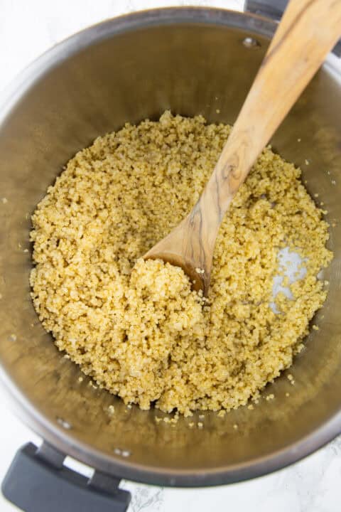 freshly cooked quinoa in an Instant Pot with a wooden spoon on a marble countertop