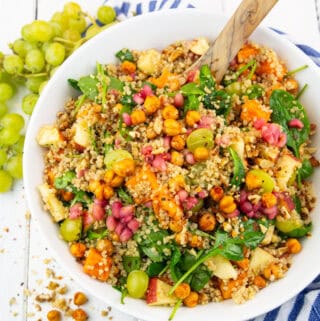 a white bowl with fall quinoa salad with sweet potato on a white wooden board with grapes in the background