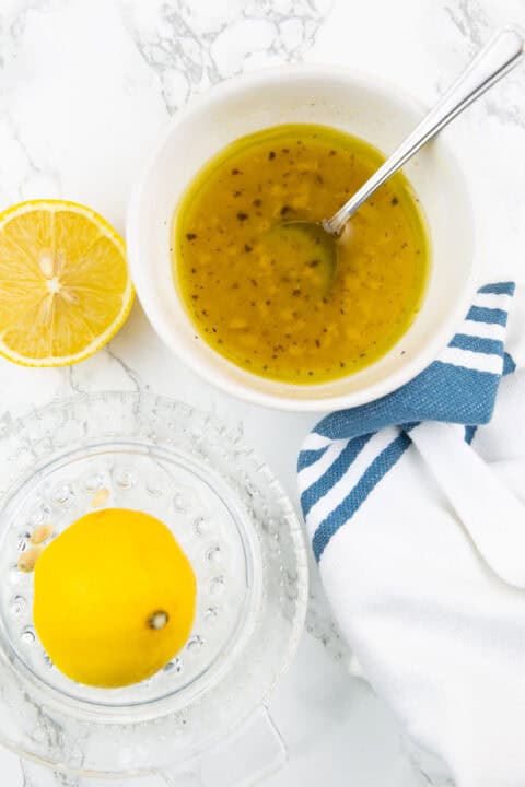 a small with bowl with dressing on a marble countertop with a lemon squeezer and two lemon halves on the side