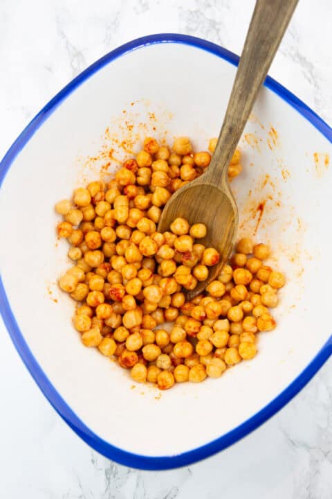a white bowl with chickpeas covered in spices and olive oil with a wooden spoon