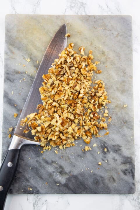 chopped walnuts on marble chopping board with a large knife on the side