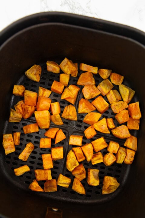 crispy sweet potato cubes in a black air fryer basket on a marble countertop