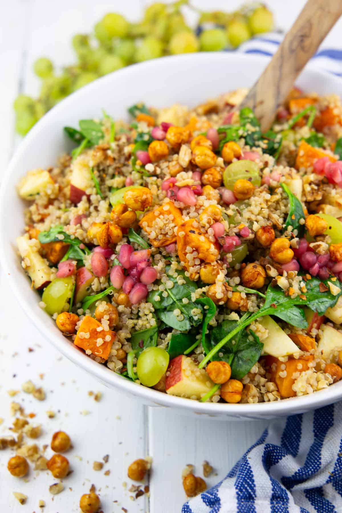 a white bowl with quinoa salad with sweet potato and grapes on a white wooden board