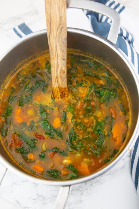 Vegan Tuscan white bean soup with carrots, sun-dried tomatoes, and baby spinach in a pot