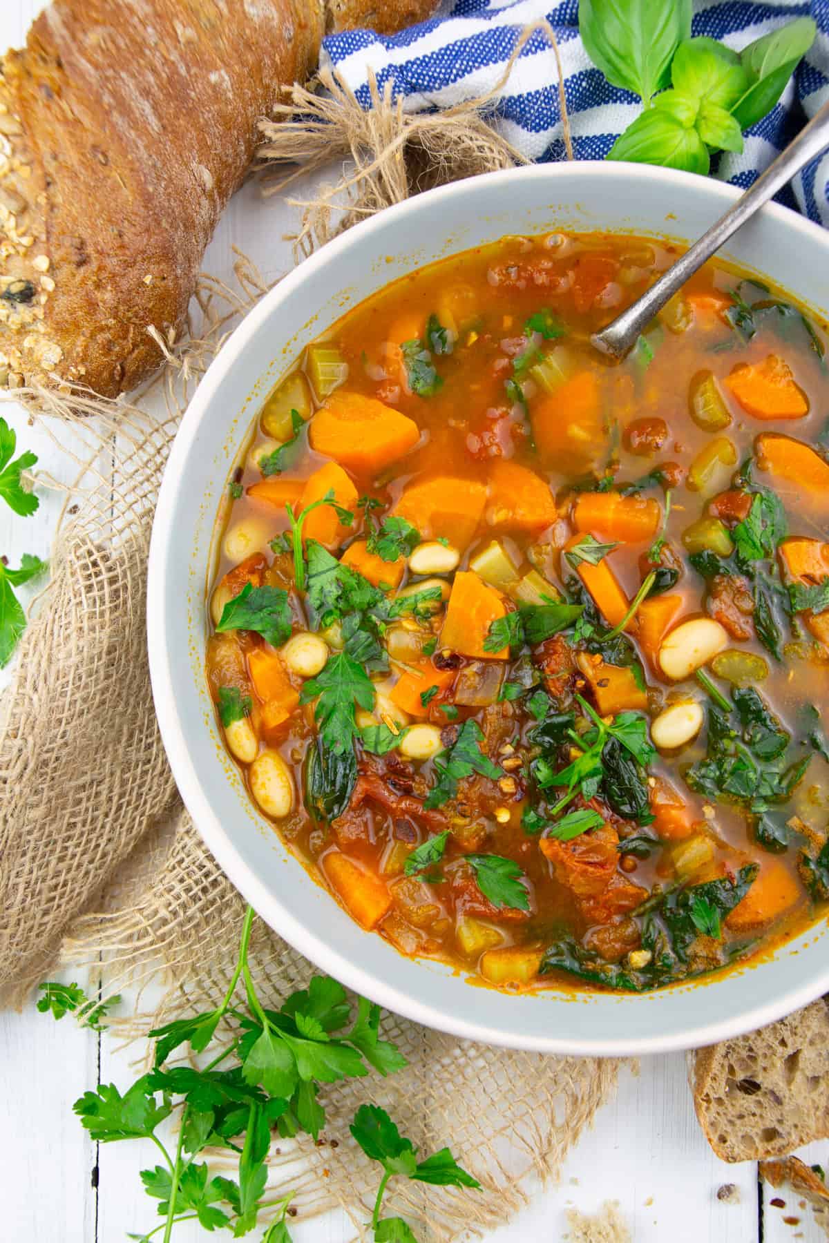 a bowl with Tuscan white bean soup with spinach on a white wooden board with bread in the background