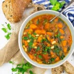 a bowl with Tuscan white bean soup with spinach on a white wooden board with bread in the background
