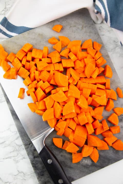 chopped carrots on a marble chopping board with a large knife on the side
