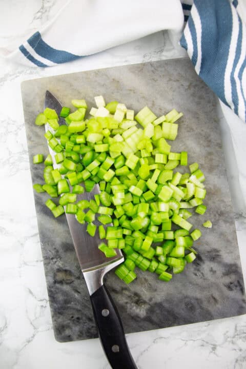 chopped celery on a chopping board with a large knife on the side
