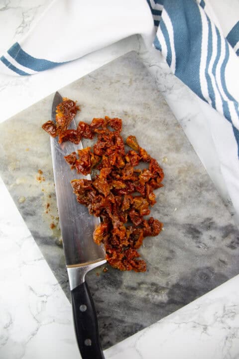 chopped sun-dried tomatoes on a marble chopping board with a knife on the side
