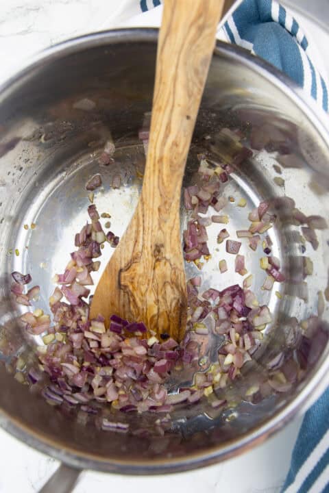 a large pot with sautéed onion and garlic with a wooden spoon